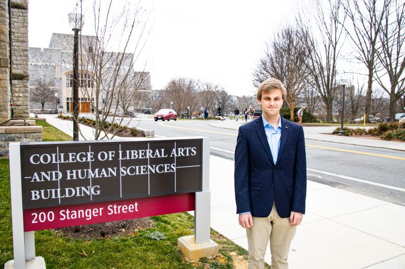 Jonathan Falls stands next to the College of Liberal Arts and Human Sciences building sign.