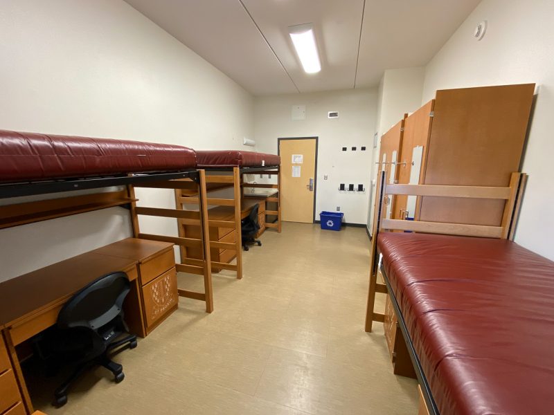 The inside of a traditional-style room in Pearson Hall East, with three lofted beds, desks, chairs, wardrobes and a small sink and mirror.